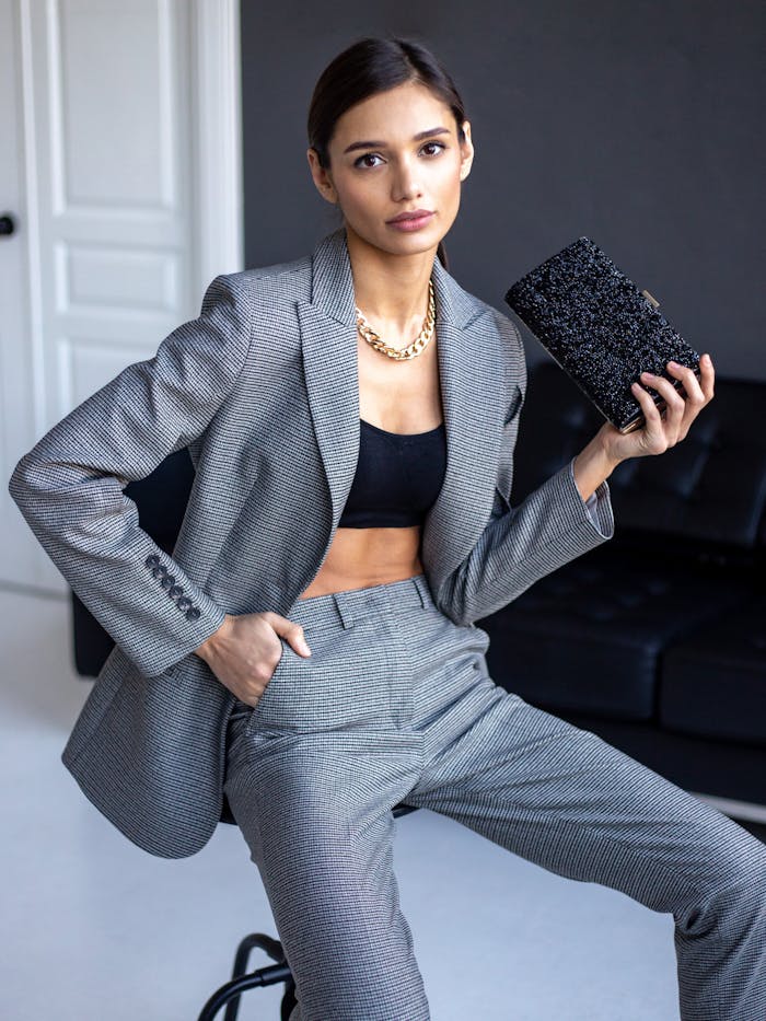 Elegant woman wearing a grey blazer and crop top, holding a textured clutch indoors.